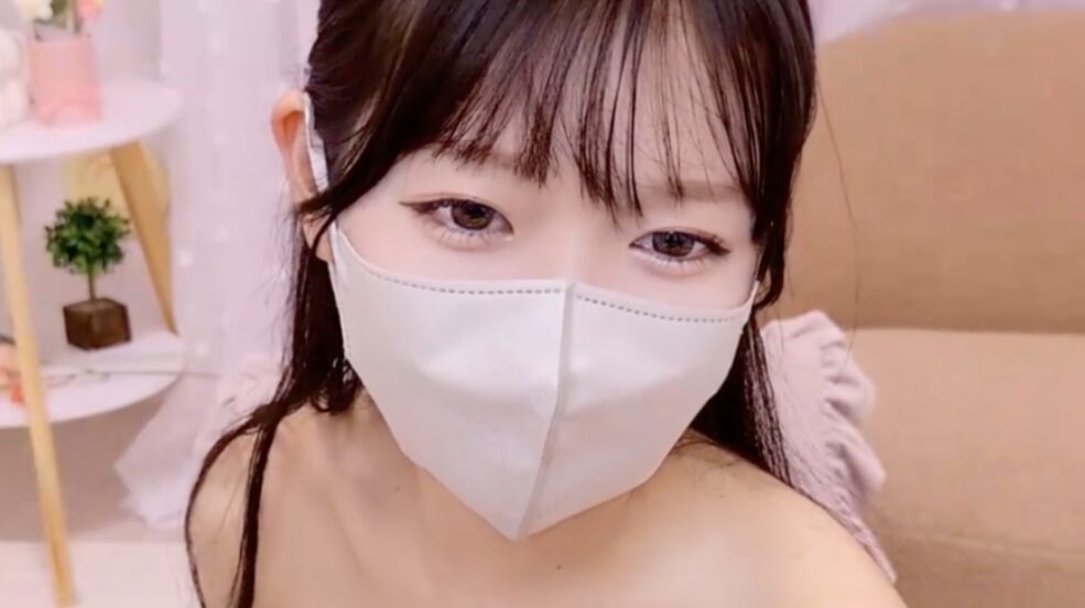 xxMeno Japanese cam girl on Stripchat wearing a white mask with big expressive eyes in a soft pastel room